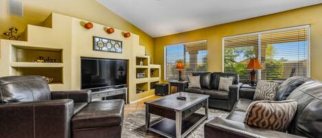 A living room with a flat-screen TV, leather sofas, a coffee table, and a ceiling fan.