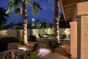 An outdoor patio area with a pool, lounge chairs, and palm trees. - Dog-friendly home with pool, firepit, fast WiFi, central AC, & washer/dryer (Goodyear)