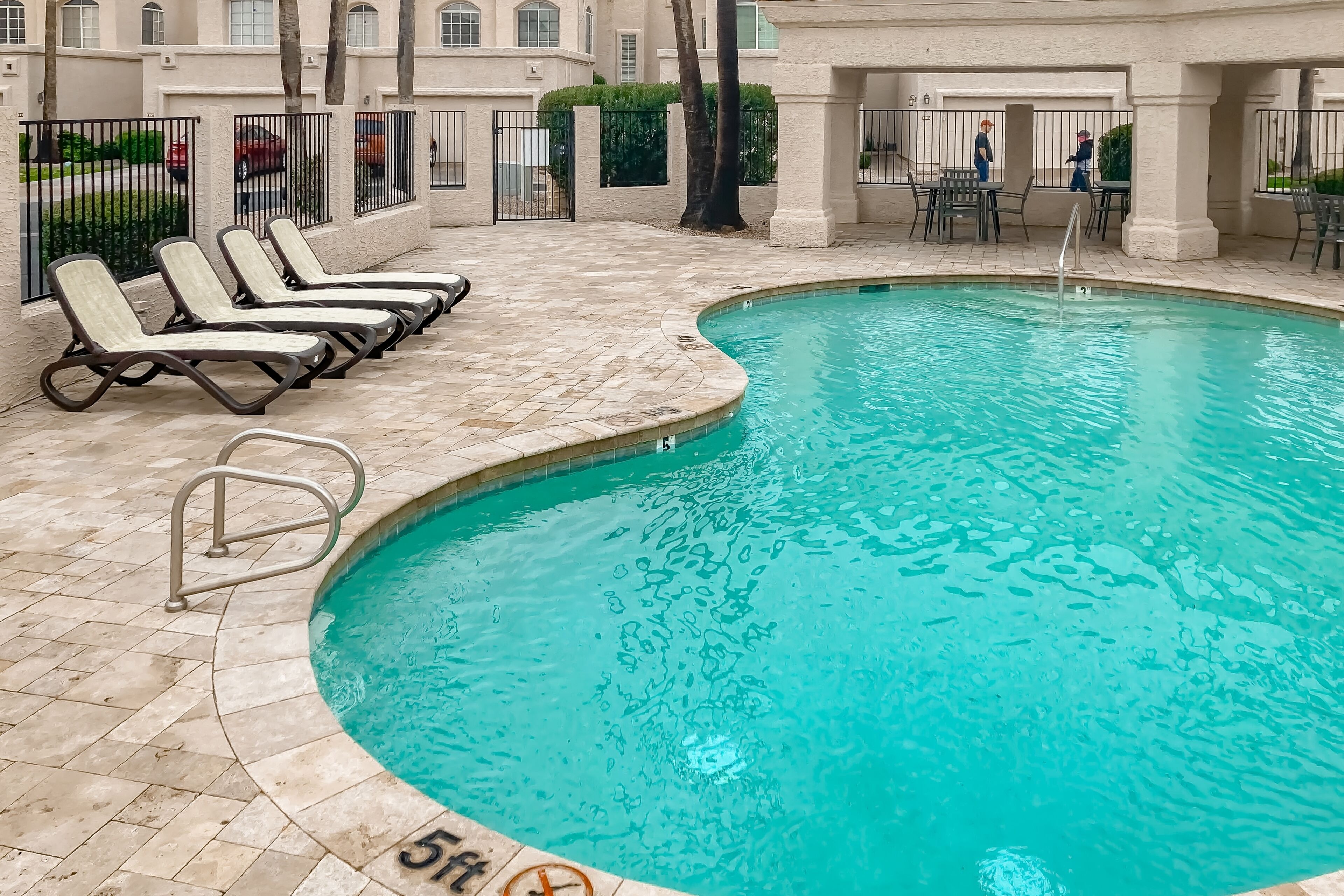 A swimming pool with lounge chairs and a tiled deck.