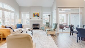 A spacious living room with a fireplace, a dining area, and large windows offering a view of the outside. - Lake view desert stay with pool, patio, grill, & smart TVs - snowbird-friendly (Gilbert)