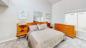 A bedroom with a large bed, wooden nightstands, a dresser, and a window with a view. - Lake view desert stay with pool, patio, grill, & smart TVs - snowbird-friendly (Gilbert)