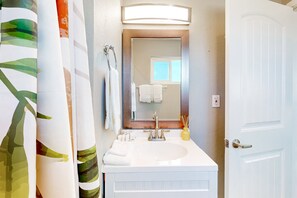A bathroom with a white sink, a mirror, and a door. - Well-equipped modern home with mountain views, washer/dryer, full kitchen, & AC (Joshua Tree)