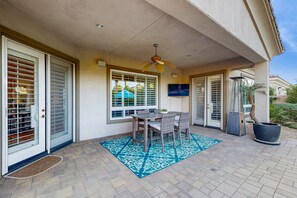 Une terrasse couverte avec une table et des chaises, un ventilateur de plafond et un téléviseur fixé au mur.