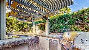 Eine Außenküche mit Grill, Spüle und einer Pergola.