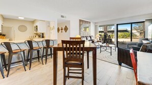 Une cuisine moderne avec un coin repas, un salon doté d’un canapé et d’une table basse, et une grande porte-fenêtre coulissante donnant sur une terrasse extérieure.