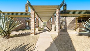 Une allée couverte, avec des piliers en briques et un auvent rayé, mène à un bâtiment dont la façade est également en briques.