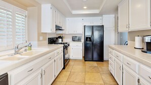 A modern kitchen with white cabinets, a black refrigerator, a stove, and a sink. - Beautiful home with private pool, enclosed backyard & mountain view (Indian Wells)