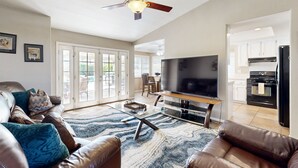 A living room with a leather sofa, a flat-screen TV, a coffee table, and a ceiling fan. - Beautiful home with private pool, enclosed backyard & mountain view (Indian Wells)