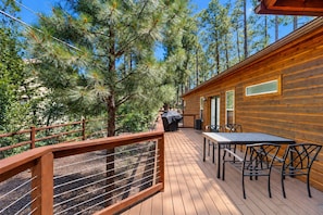 A wooden deck with outdoor furniture, surrounded by trees. - Dog-friendly forested home with wraparound deck, pool table (Pinetop)