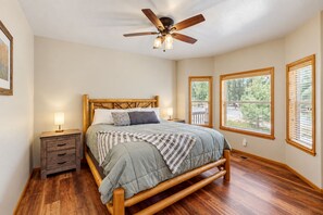 A bedroom with a wooden bed, bedside lamps, a ceiling fan, and large windows with blinds. - Dog-friendly forested home with wraparound deck, pool table (Pinetop)
