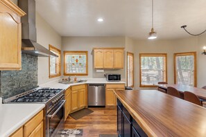 A modern kitchen with a gas stove, stainless steel appliances, wooden cabinets, and a large island with seating. - Dog-friendly forested home with wraparound deck, pool table (Pinetop)
