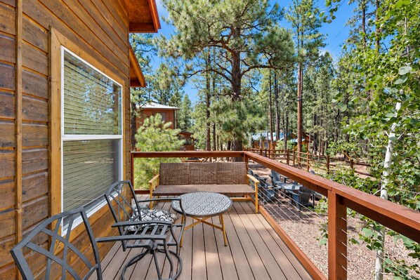 Une terrasse en bois, aménagée avec du mobilier d’extérieur, notamment une table et des chaises, donnant sur une zone boisée.