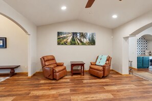 A spacious living room with two leather armchairs, a small table, and a large painting on the wall. - Dog-friendly forested home with wraparound deck, pool table (Pinetop)