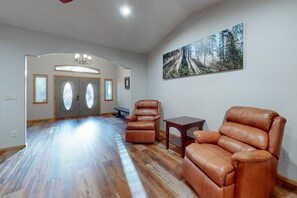 A spacious living room with hardwood flooring, leather recliners, a small table, and a large forest-themed painting on the wall. - Dog-friendly forested home with wraparound deck, pool table (Pinetop)
