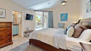Un dormitorio con cama, cómoda, televisor y puerta corrediza de vidrio a un balcón.