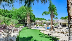 Campo de golf con un putting green, palmeras y una zona de piscina.