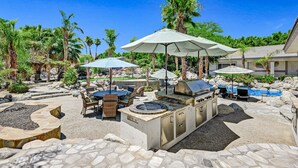 Un patio con una parrilla, mobiliario exterior y sombrillas.