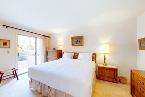 A bedroom with a large bed, a wooden nightstand with a lamp, a wooden dresser, a bench, and a sliding glass door leading to an outdoor area. - Inviting townhouse with pool, enclosed yard, patio, mountain view & W/D (Tucson)