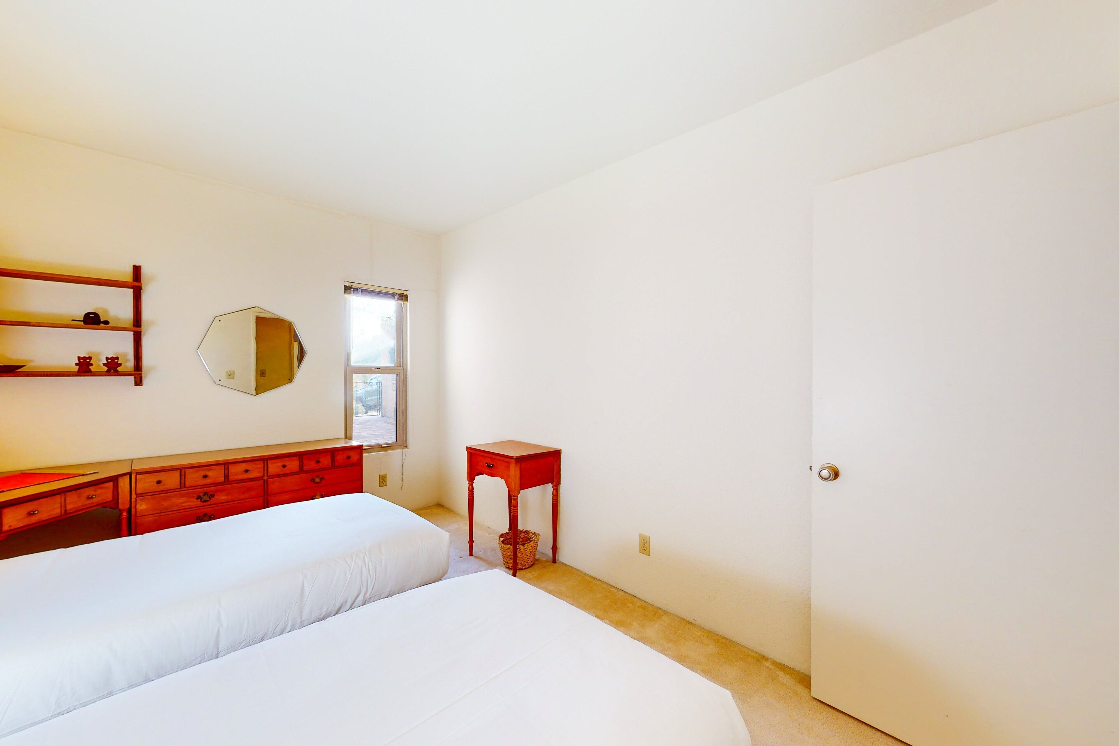 A bedroom with two beds, a dresser, a mirror, and a door.