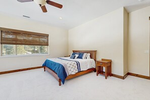 A bedroom with a bed, a nightstand, a ceiling fan, and a window with blinds.