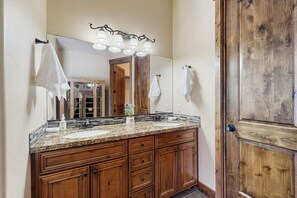 Un baño con tocador de madera, dos lavamanos, un espejo grande y una puerta de madera.