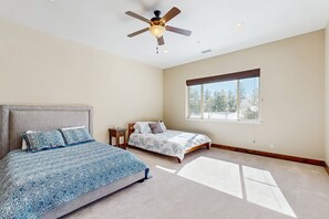 A bedroom with two beds, a ceiling fan, and a large window.
