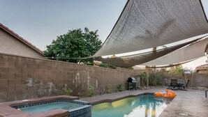 Ein Schwimmbecken mit Whirlpool und einem schwimmenden Spielzeug, umgeben von einer Ziegelmauer und einem schattigen Bereich.