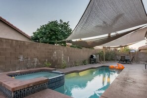 A swimming pool with a hot tub and a floating toy, surrounded by a brick wall and a shaded area. - Mountain view home with pool, spa and dog friendly (La Quinta)