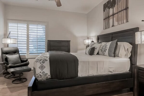 A bedroom with a bed, a chair, a nightstand, and a window with blinds. - Mountain view home with pool, spa and dog friendly (La Quinta)