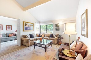 Ein geräumiges Wohnzimmer mit hohen Decken, einem Glastisch und verschiedenen Sitzgelegenheiten, darunter Sofas und Sessel.