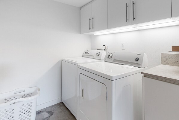 A laundry area with a front-loading washer and dryer, a drying rack, and a countertop with a sink. - Family-Friendly Condo w/ Mountain Views, Private Pool (Palm Springs)