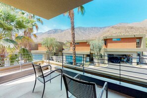 A balcony with two chairs, a pool, and a building with a desert backdrop. - Family-Friendly Condo w/ Mountain Views, Private Pool (Palm Springs)