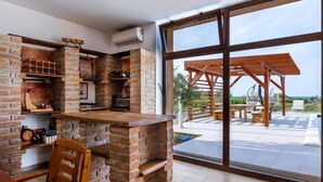 A modern kitchen with brick walls, wooden shelves, and a large window overlooking a patio area.