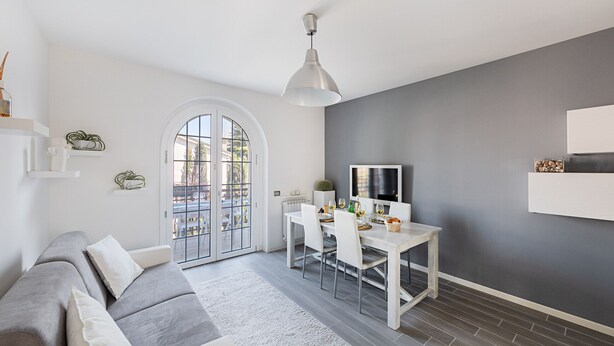 Una sala moderna con un sofá gris, una mesa de comedor blanca y una pared de acento gris.