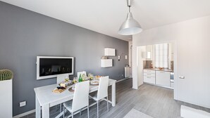 Un comedor moderno con una mesa blanca, sillas y un televisor en la pared.