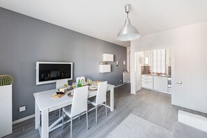 Ein moderner Essbereich mit einem weißen Tisch, Stühlen und einem Fernseher an der Wand.