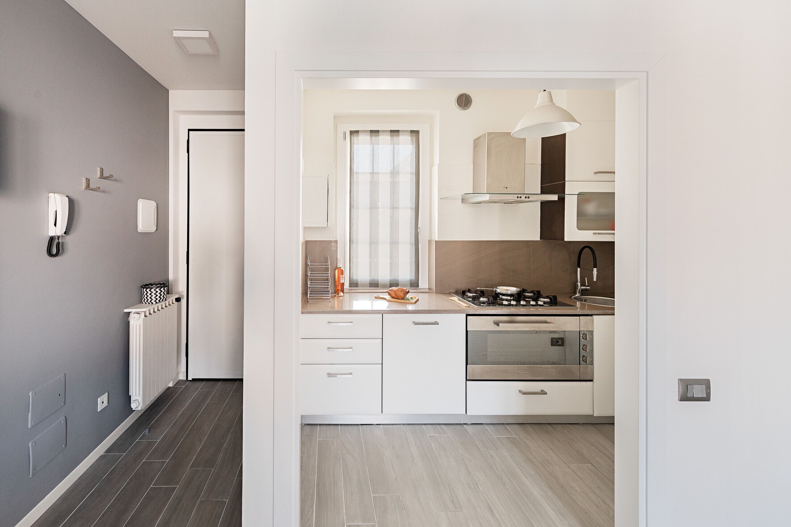 Una cocina moderna con armarios blancos, electrodomésticos de acero inoxidable y un ventanal con cortinas.