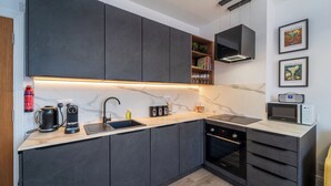 A modern kitchen with dark cabinets, a marble countertop, a built-in oven, and a microwave. - Modern 2 En-Suite Bedrooms Worcester, Free Parking (Worcestershire)