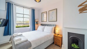 A bedroom with a bed, a nightstand, a television, a fireplace, and a window with curtains. - Modern 2 En-Suite Bedrooms Worcester, Free Parking (Worcestershire)