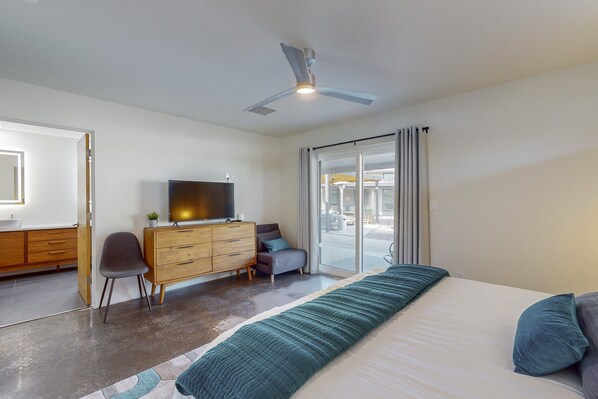 Une chambre moderne avec un grand lit, un ventilateur de plafond, une télévision, une commode et une vue sur l’extérieur grâce à une porte coulissante.