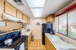 A compact kitchen with a gas stove, oven, and a black refrigerator. - Resort living golf getaway with country club, near Joshua Tree National Park (Palm Desert)