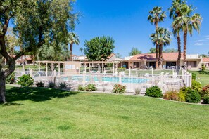 A pool area with a fenced deck, surrounded by palm trees and a well-maintained lawn. - Resort living golf getaway with country club, near Joshua Tree National Park (Palm Desert)