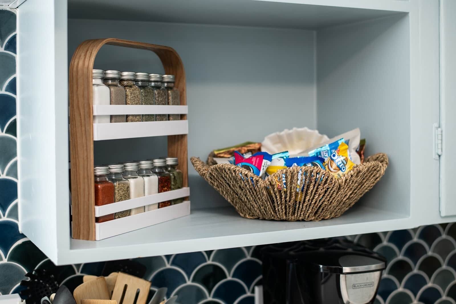 A kitchen with a wooden spice rack, a woven basket with snacks, and a coffee maker.
