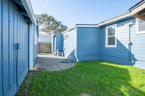 Un jardin à l’arrière d’une maison, avec une pelouse, une clôture en bois et une maison bleue.