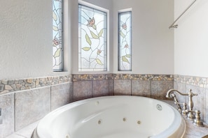 Ein Badezimmer mit einer großen Badewanne, einem Mosaik-Fliesenrückwand und Buntglasfenstern.