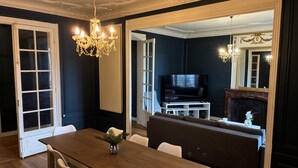 A dining area with a wooden table, white chairs, a chandelier, a television, and a fireplace.