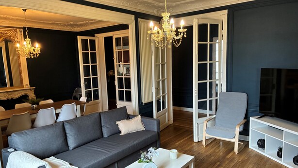 A modern living room with a grey sofa, a white coffee table, a grey armchair, and a TV stand.