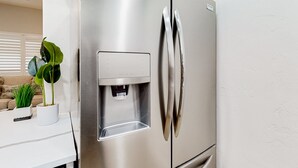 A stainless steel refrigerator with a water dispenser, a white countertop, and a potted plant.