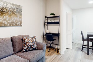 A living room with a grey sofa, a patterned pillow, a black office chair, a desk with a computer, and a bookshelf with plants. - Chic dog-friendly condo with pool, central AC, washer/dryer, & grill (Tucson)