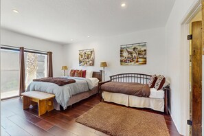 Ein Schlafzimmer mit zwei Betten, einer hölzernen Bank, einem großen Fenster und zwei Wandleuchten.